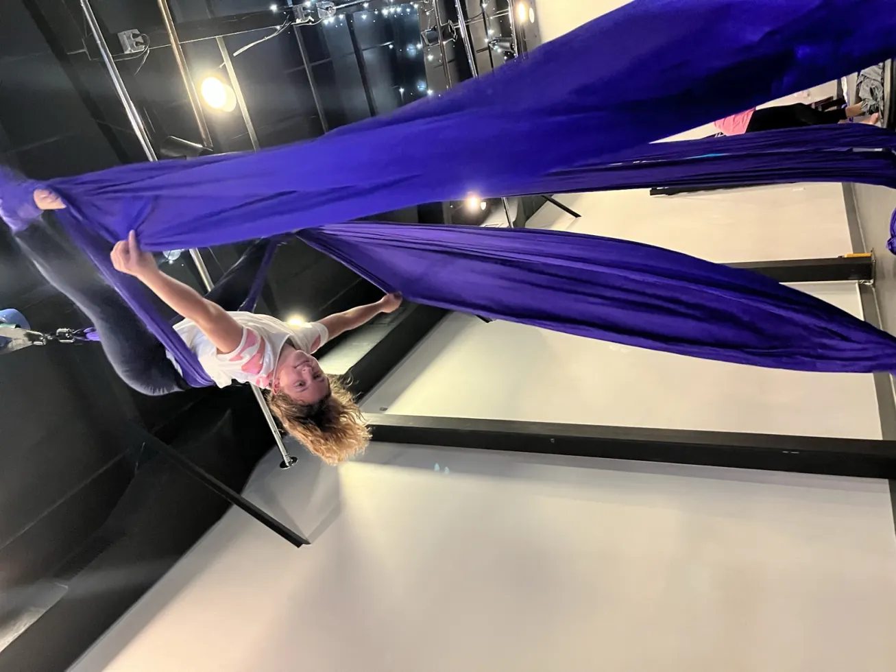 Ruby hanging upside down from purple aerial silks in class