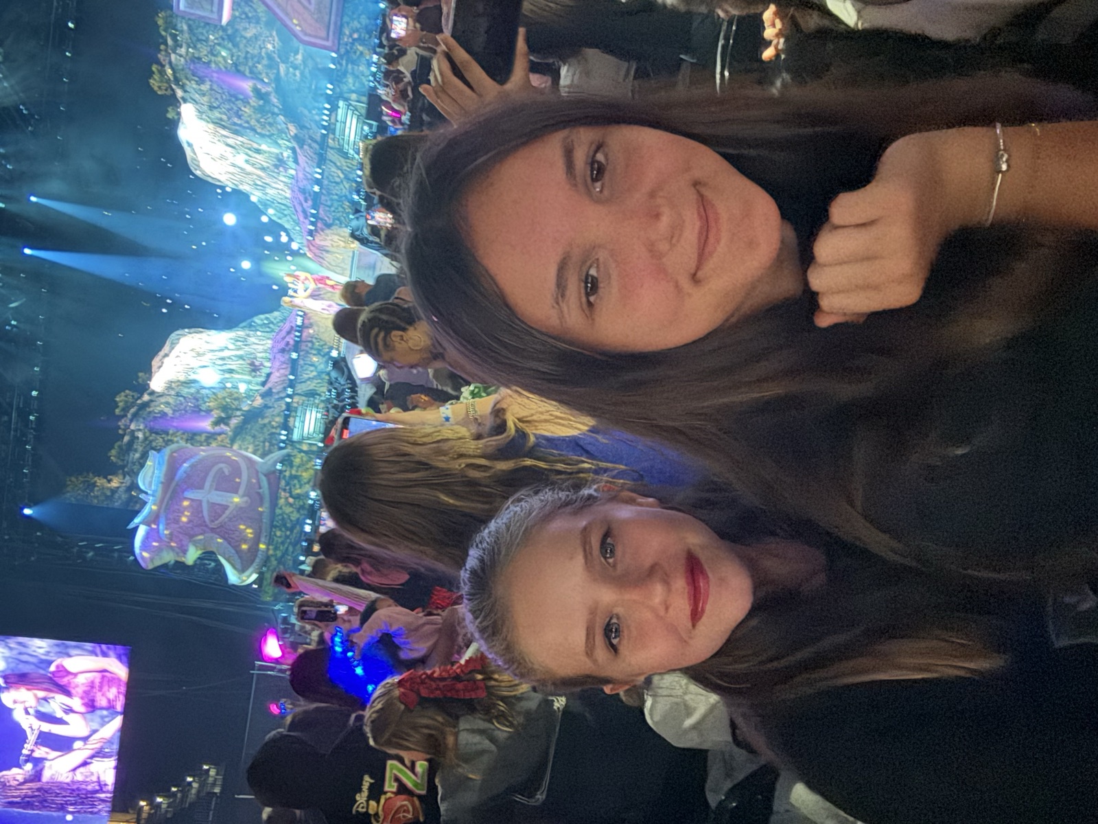 Ruby and a friend in the crowd at an arena show, stage lit behind them