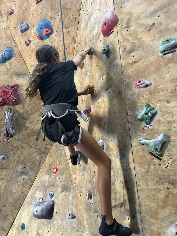 Ruby reaching for a hold on a climbing wall