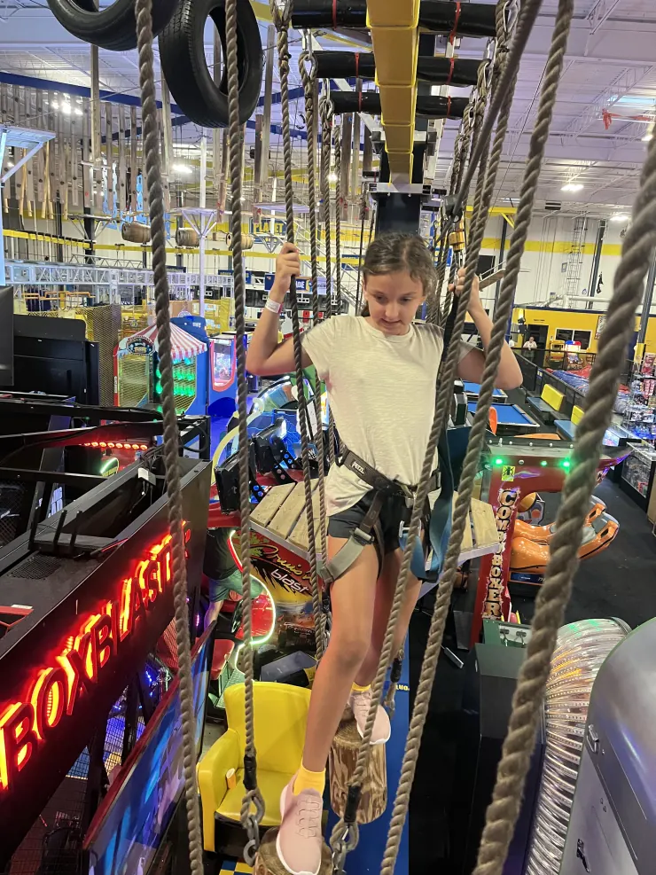 Ruby balancing on a rope course above an arcade floor