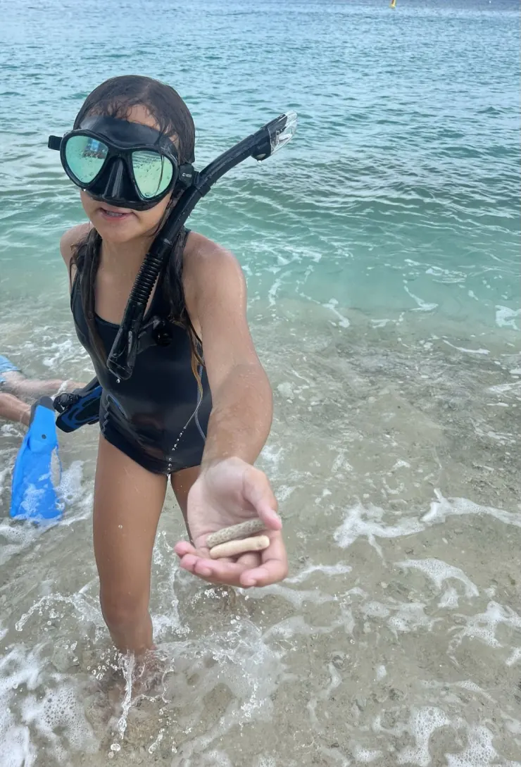 Ruby in a snorkel mask holding a shell at the shore