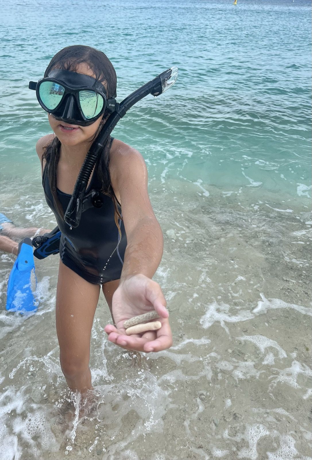 Ruby in a snorkel mask holding a shell at the shore