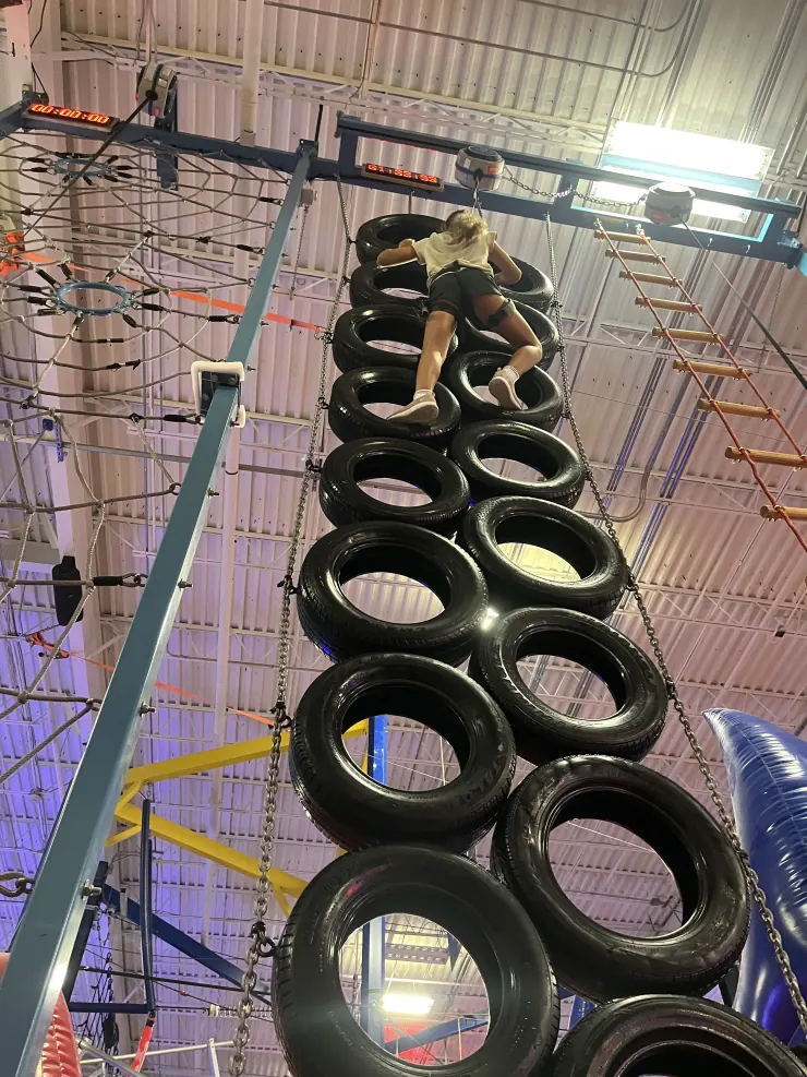 Ruby climbing a wall of stacked tires on an indoor ropes course