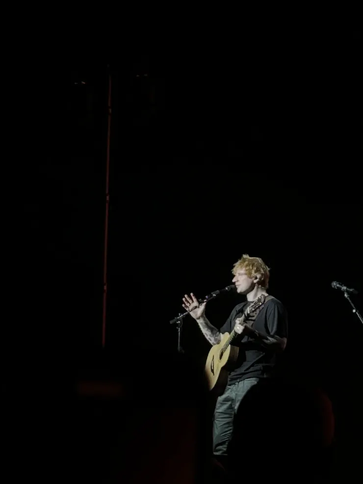 Ed Sheeran singing into the microphone, guitar in hand