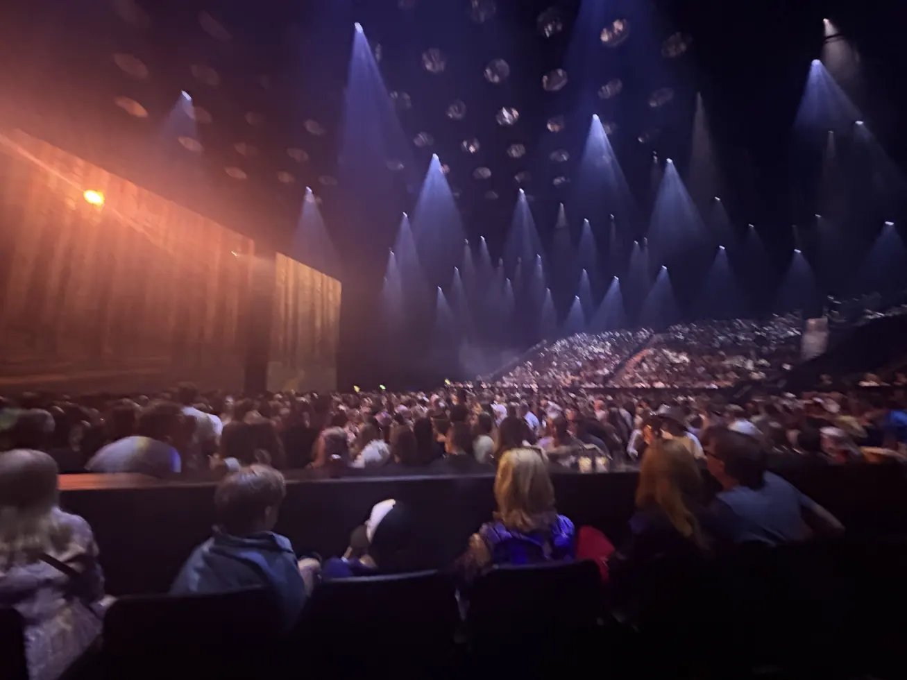 The arena filling up, spotlights angled over the seated crowd