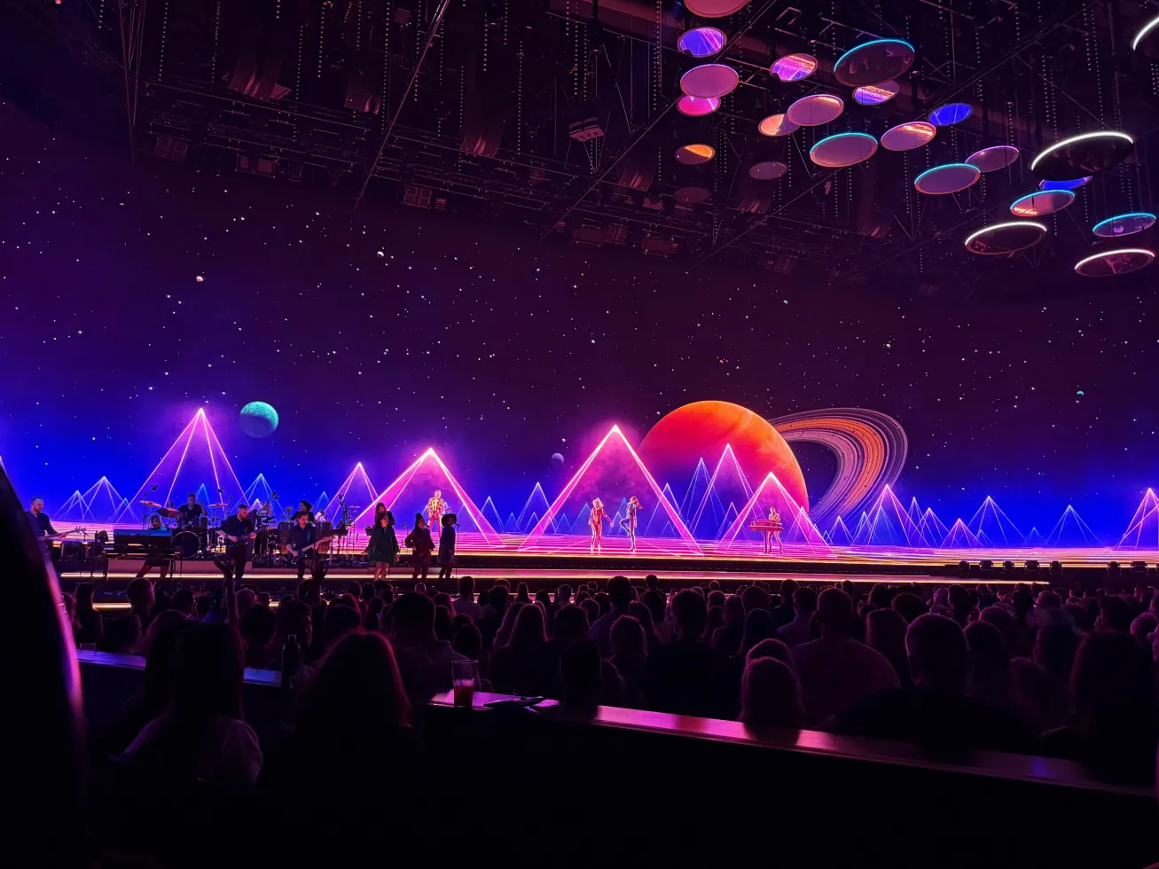 The stage lit purple and blue with planets and rings behind the performers