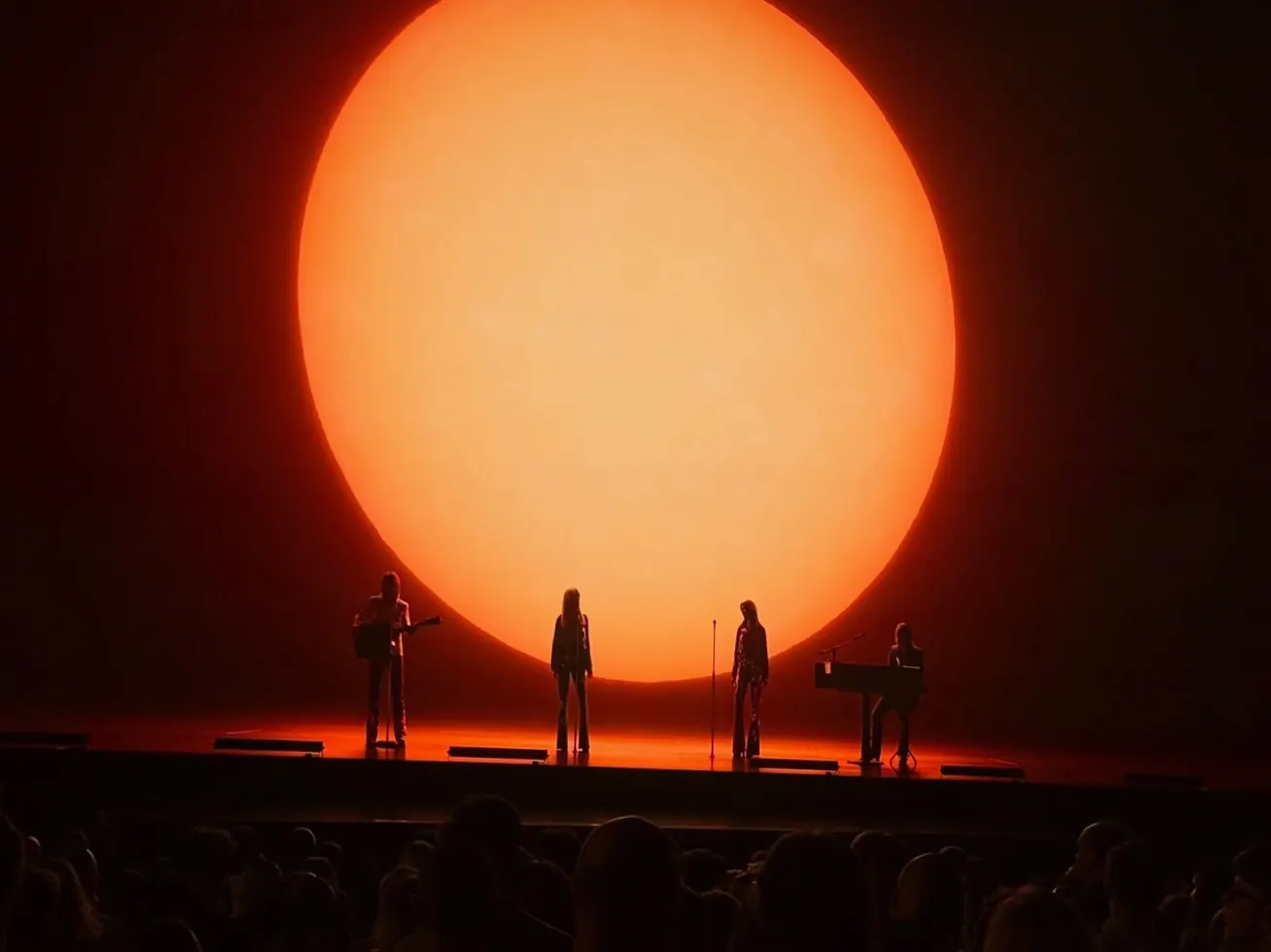 Four figures silhouetted against an enormous orange sun on stage