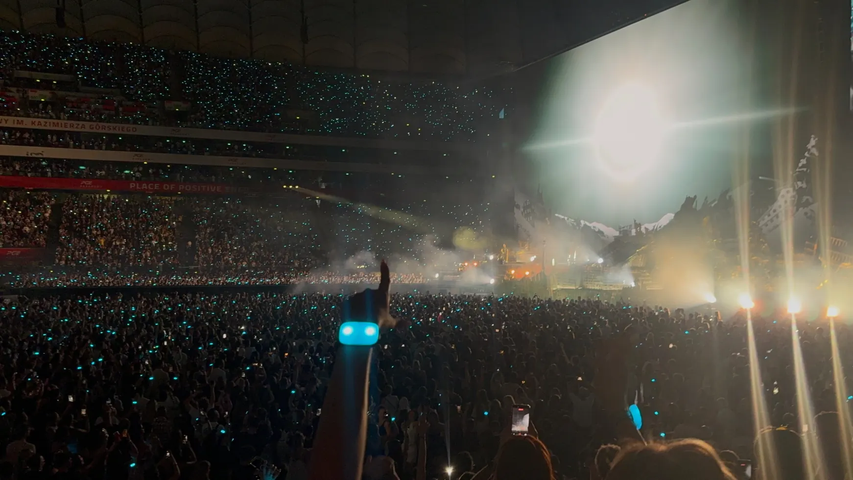 The stadium crowd lit up by light-up wristbands, smoke drifting across the floor