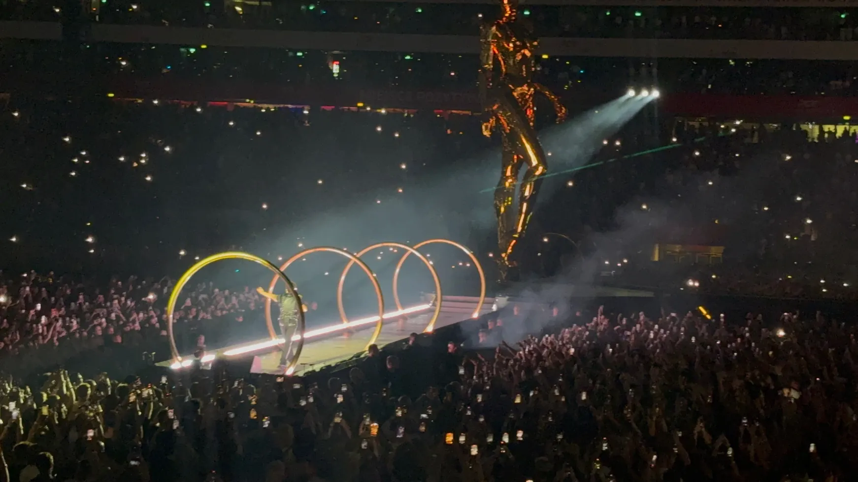 A towering golden figure on stage above lit arches and the crowd