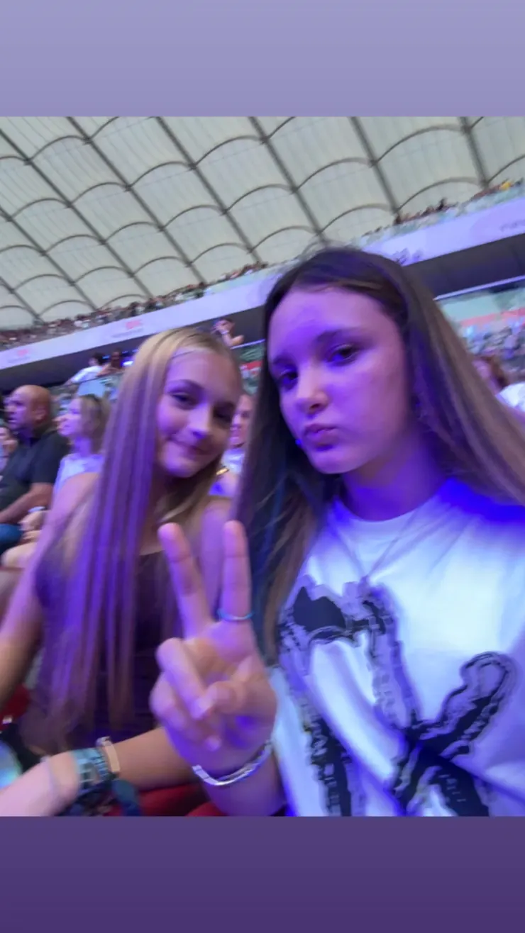 Ruby and a friend leaning in for a photo, stadium roof behind them