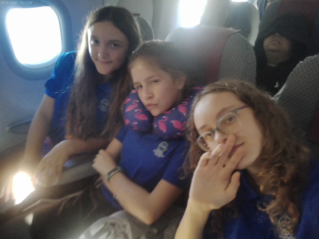 Three girls on a plane, one resting on a flamingo travel pillow