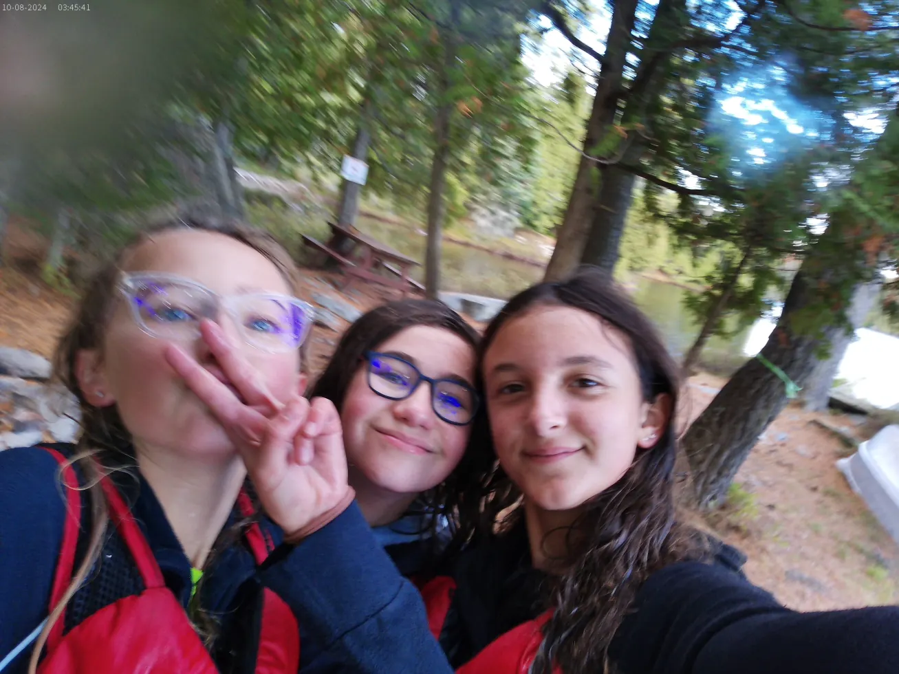 Three girls giving a peace sign by a lake in the forest