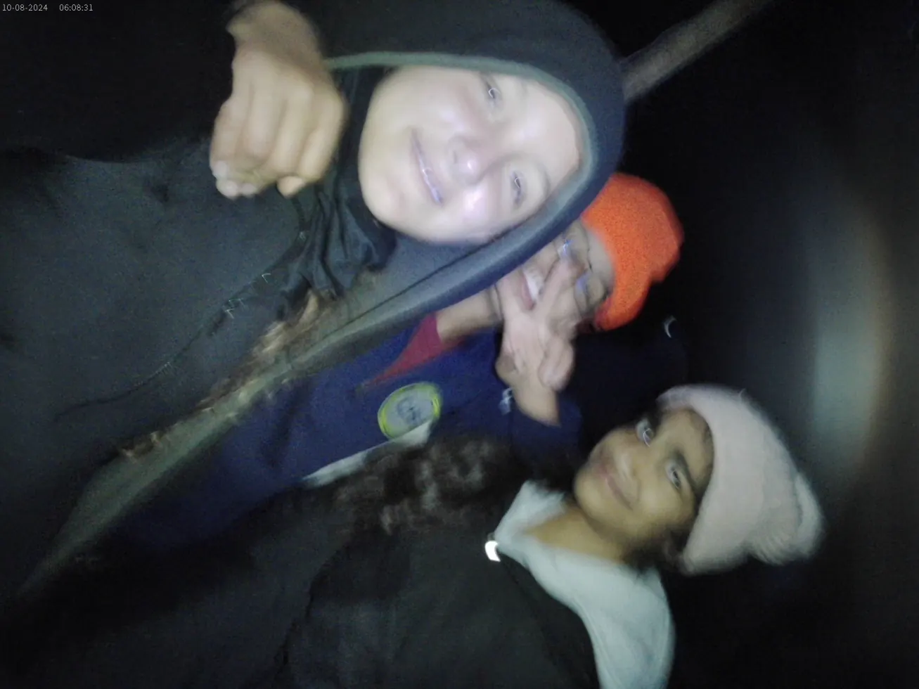 A blurry, cheerful night selfie of three campers in beanies and headlamps