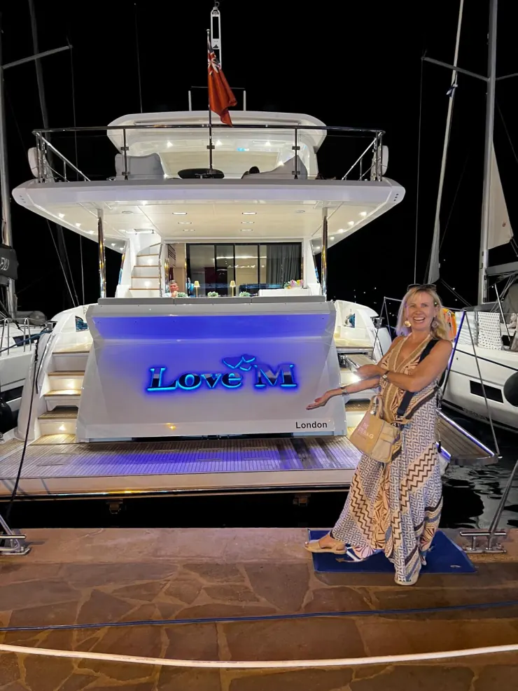 A woman posing at the stern of a yacht named Love M, moored at night