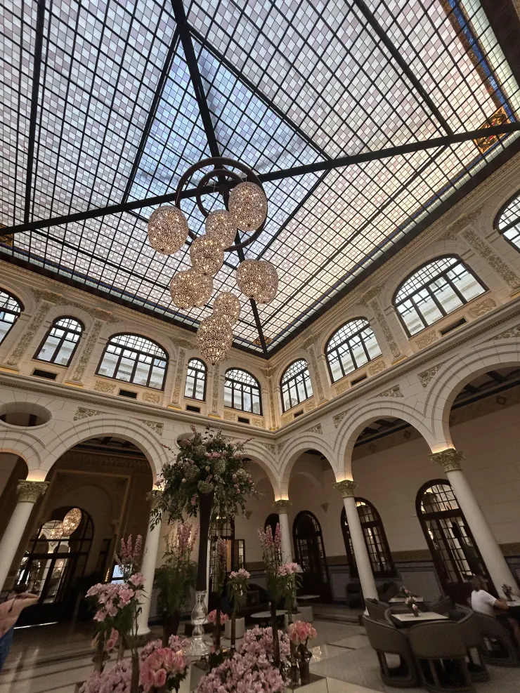 A stained-glass ceiling and chandeliers over a marble arcade hung with pink flowers