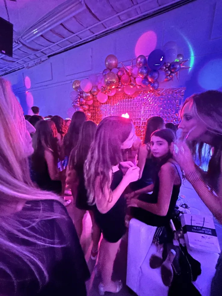 A crowded dance floor in front of a balloon-and-disco-ball backdrop