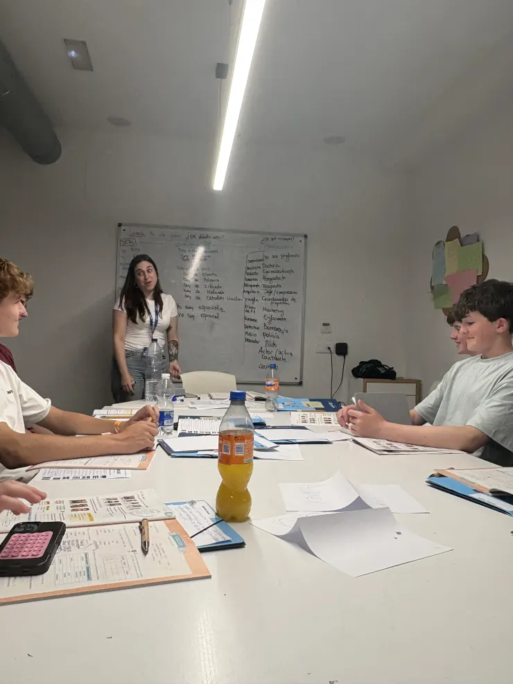 Campers in a Spanish class around a table, teacher at a whiteboard