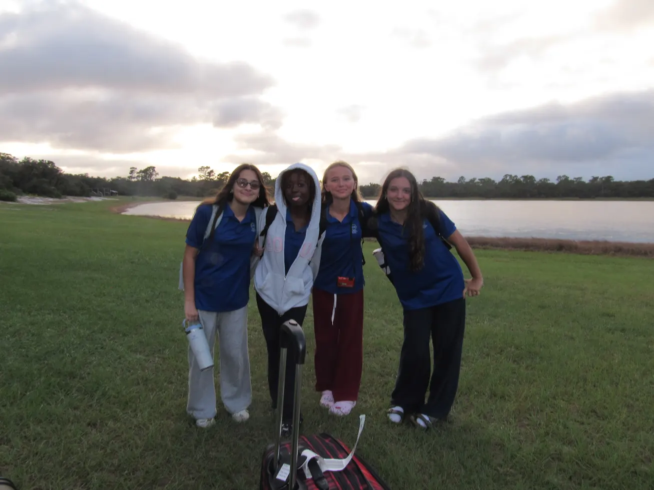Four girls with luggage on the grass at dusk, arriving at camp