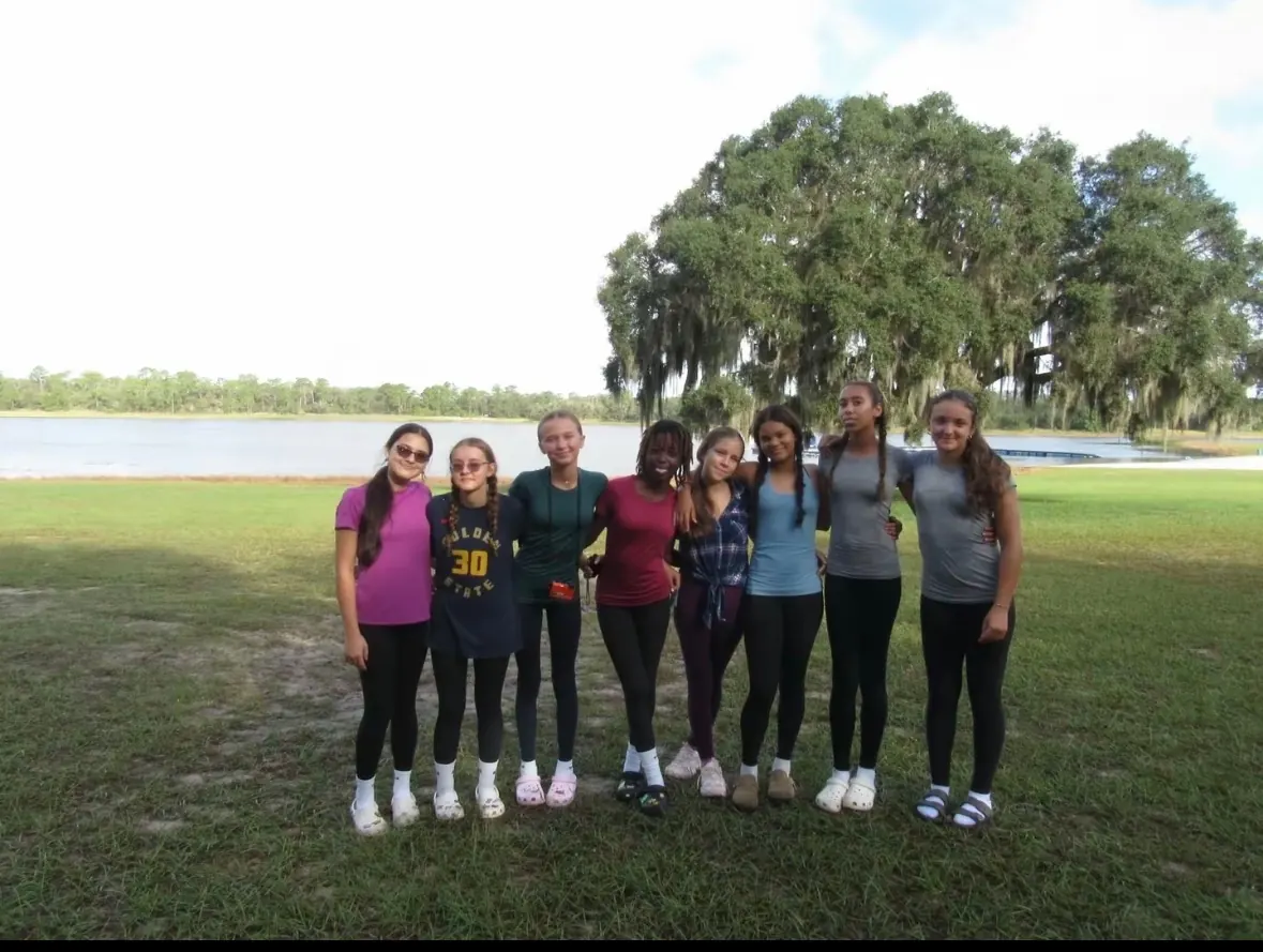 A group of eight girls posing by a lake under a huge oak tree