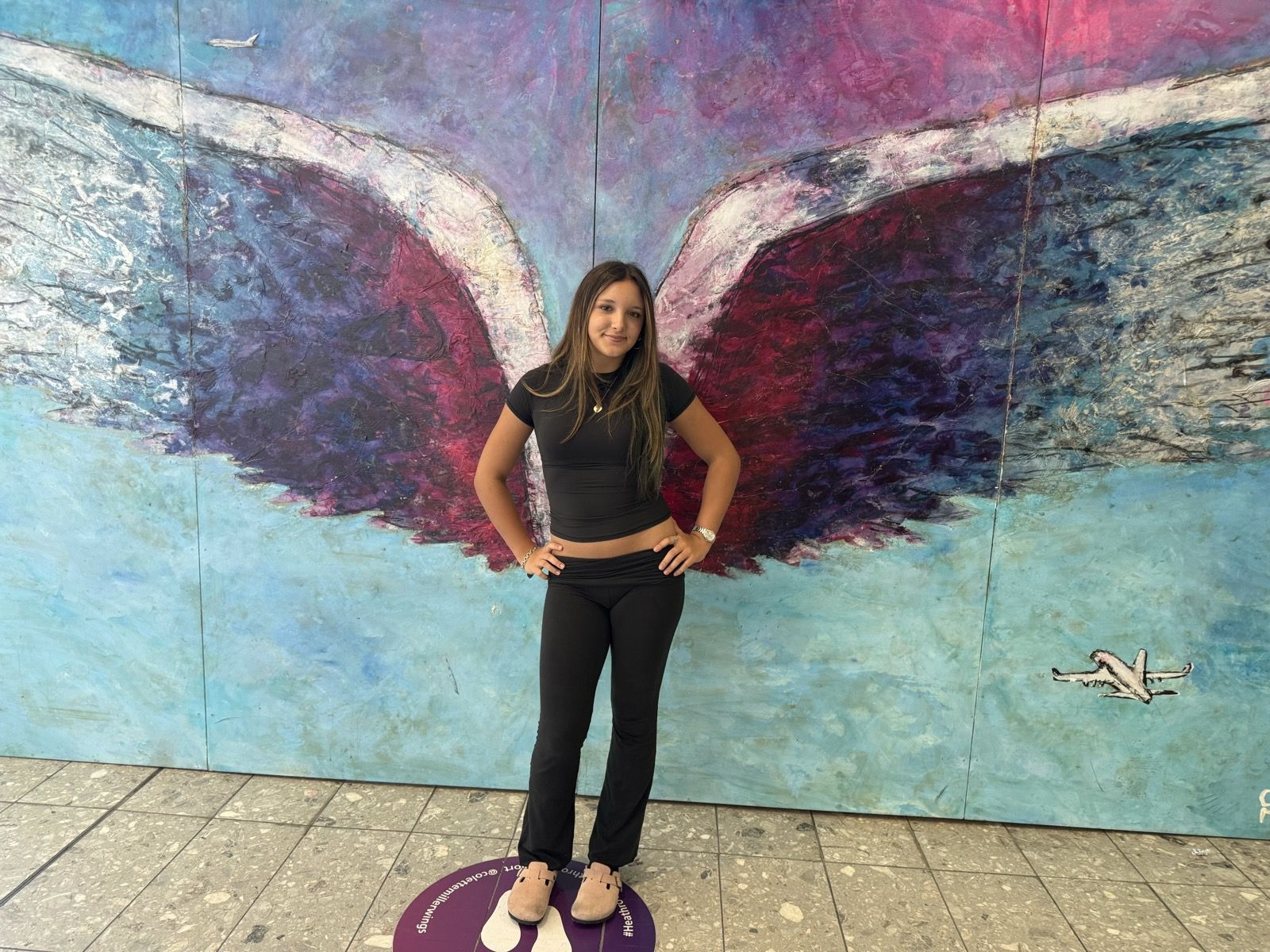 Ruby in front of a painted wings mural