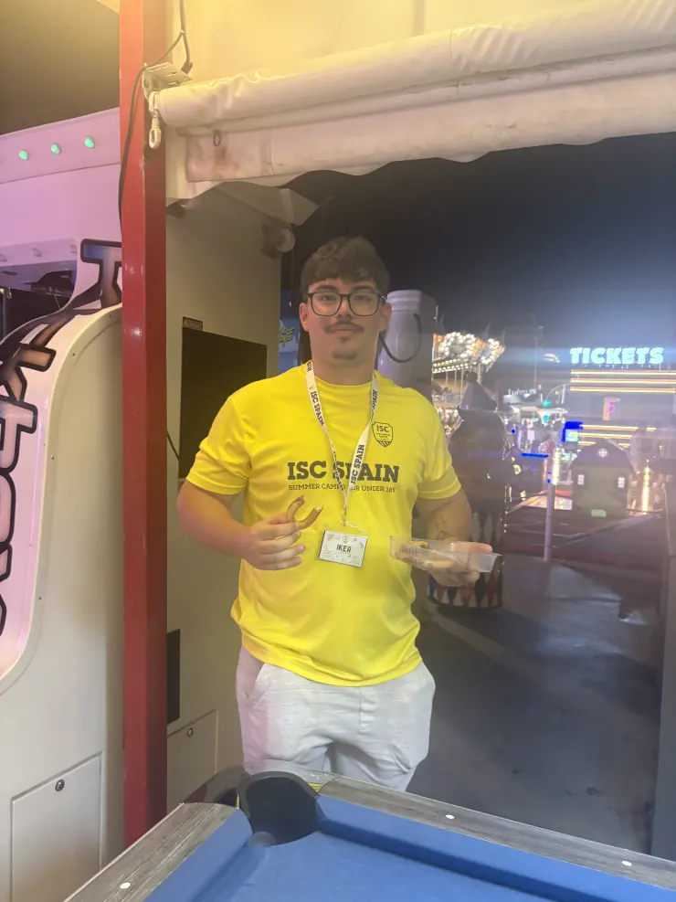 A camp counselor in a yellow ISC Spain shirt holding churros at a night fairground
