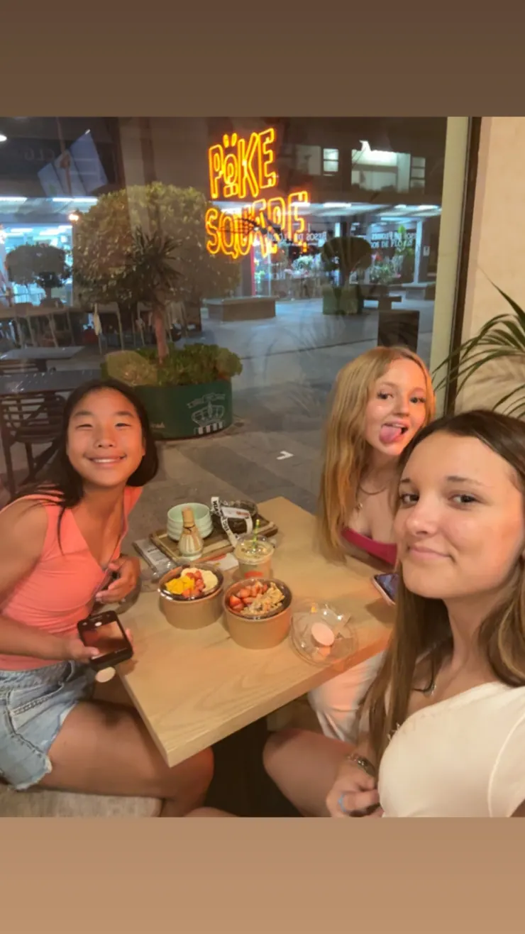 Ruby holding up a poke bowl at a restaurant table with camp friends