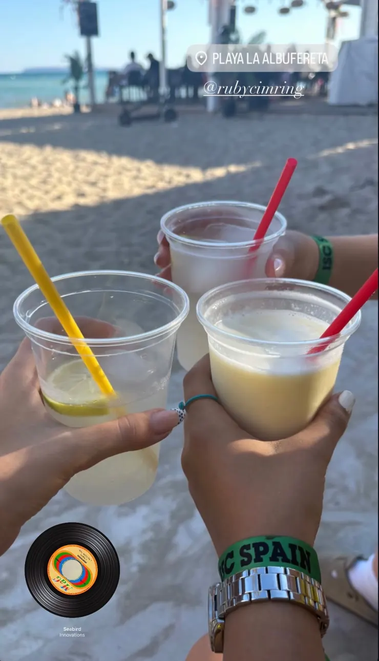 Three camp drinks held up together on the beach, ISC Spain wristbands visible