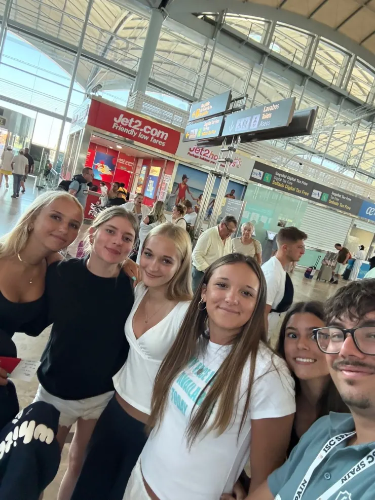 Six camp friends posing together at the airport before flying home